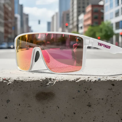 White sunglasses with pink mirrored lenses on a concrete ledge in a city