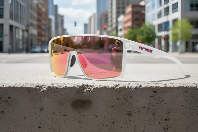 White sunglasses with pink mirrored lenses on a concrete ledge in a city