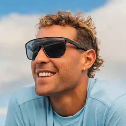 Man with curly hair wearing black sunglasses and a light blue shirt