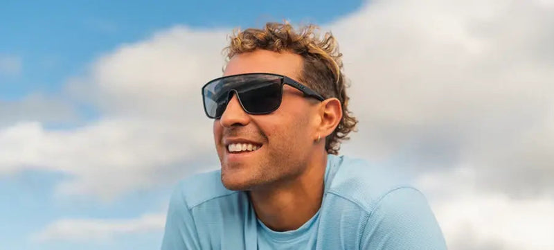 Man with curly hair wearing black sunglasses and a light blue shirt