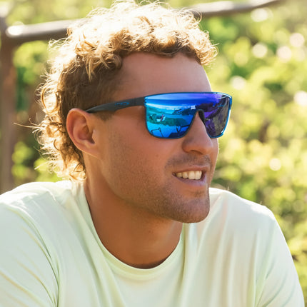 Man with curly hair wearing blue mirrored sunglasses and a light green shirt