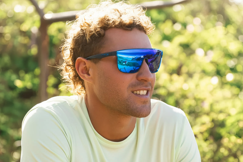 Man with curly hair wearing blue mirrored sunglasses and a light green shirt