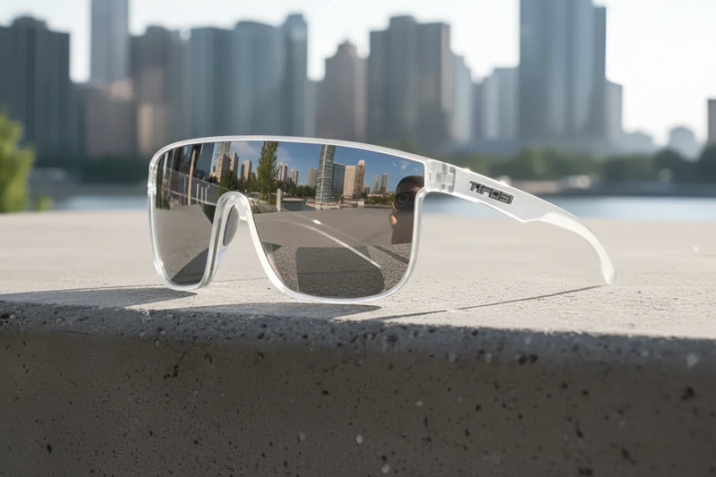 White sunglasses with reflective lenses on a concrete ledge, city skyline reflected in lenses