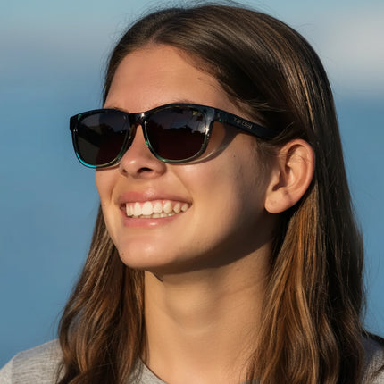 Woman wearing black and teal sunglasses with dark lenses