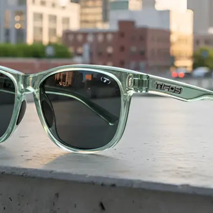 Light green sunglasses with dark lenses on a concrete ledge, city buildings and a car in the background