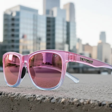 Pink sunglasses with reflective lenses on a concrete ledge, city skyline in background