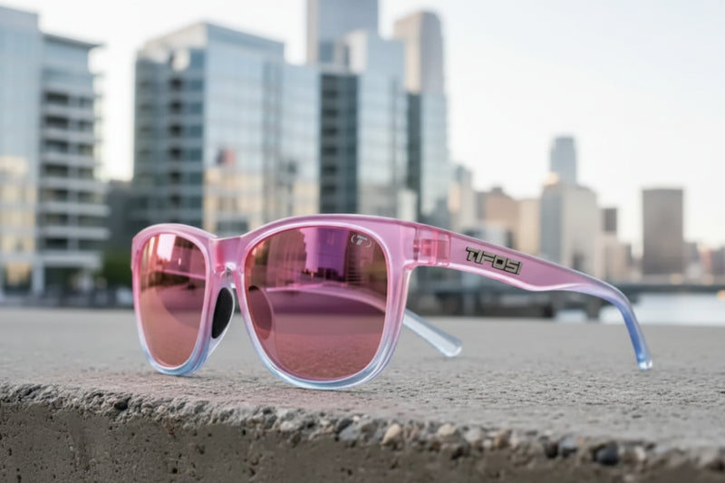 Pink sunglasses with reflective lenses on a concrete ledge, city skyline in background