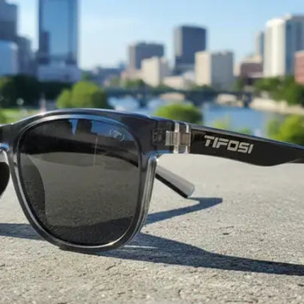 Tifosi sunglasses on a concrete surface with a city skyline and river in the background