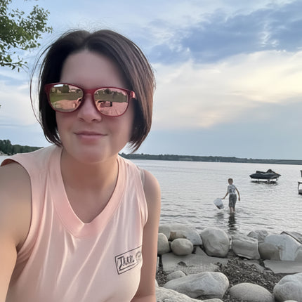 Woman in sunglasses and tank top by a lake, child in water