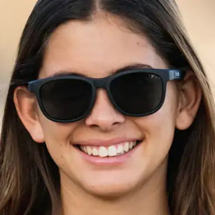 Woman with long brown hair wearing black sunglasses and smiling