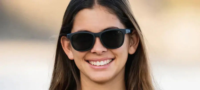 Woman with long brown hair wearing black sunglasses and smiling