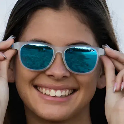 Woman smiling, adjusting blue mirrored sunglasses with both hands