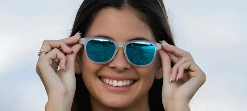 Woman smiling, adjusting blue mirrored sunglasses with both hands