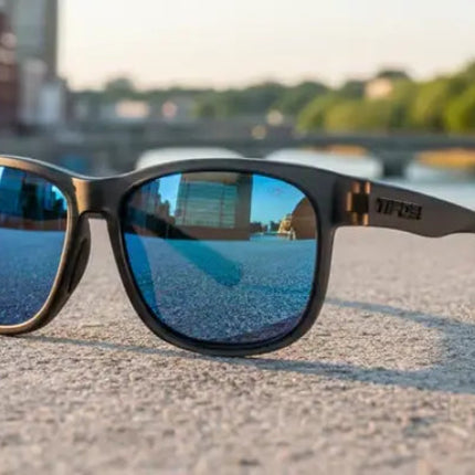 Black sunglasses with blue mirrored lenses on a concrete surface, with a city background