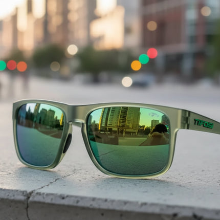 Green sunglasses with reflective lenses on a concrete ledge, city buildings and traffic lights reflected in lenses