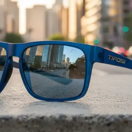 Blue sunglasses with mirrored lenses reflecting a city street and buildings