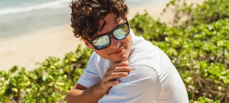 Man in sunglasses and white shirt on a beach with green foliage