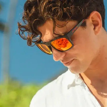Man with curly hair wearing sunglasses with orange lenses and a white shirt