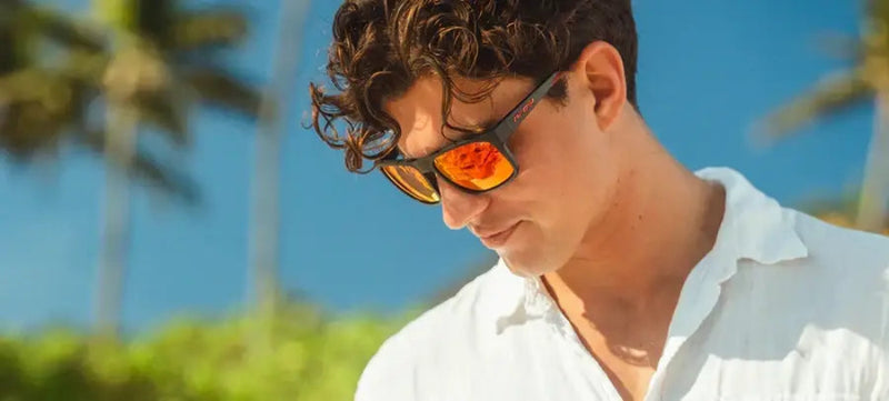 Man with curly hair wearing sunglasses with orange lenses and a white shirt