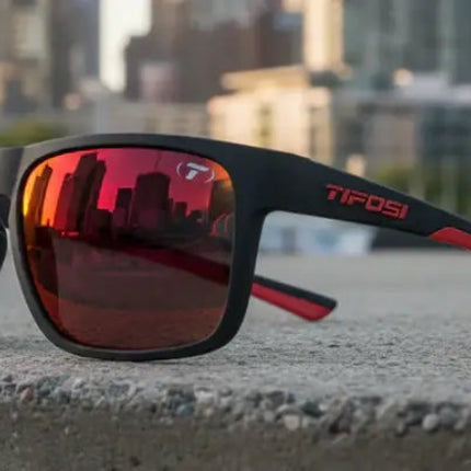 Black sunglasses with red reflective lenses and red accents on the arms, cityscape reflected in lenses