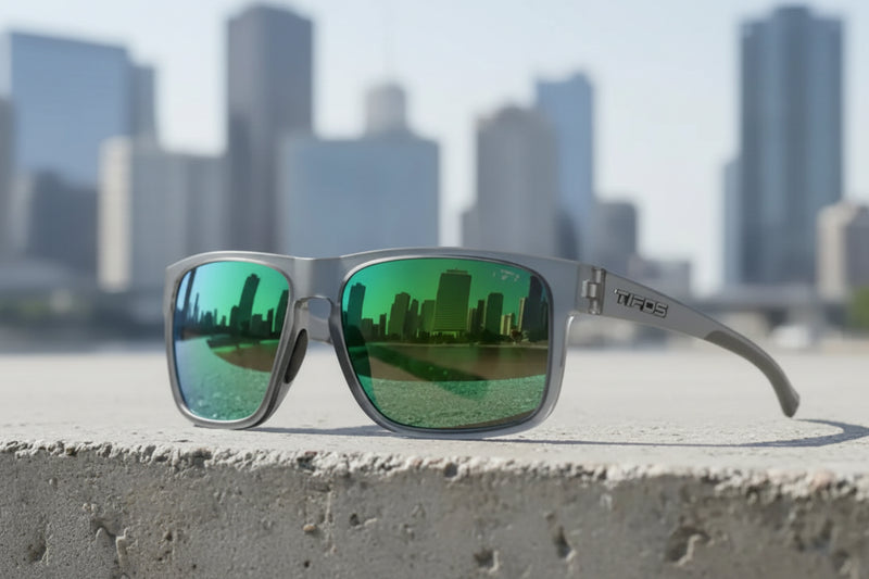 Grey sunglasses with green mirrored lenses reflecting a city skyline