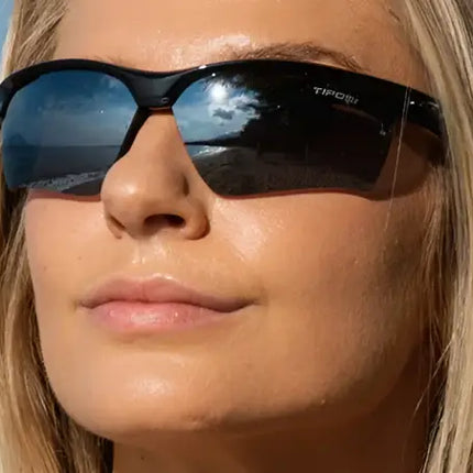 Woman wearing black sunglasses with reflective lenses, beach scene reflected in lenses