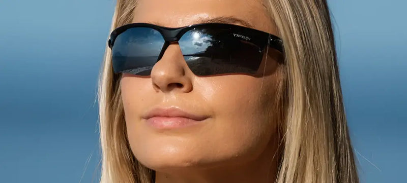 Woman wearing black sunglasses with reflective lenses, beach scene reflected in lenses