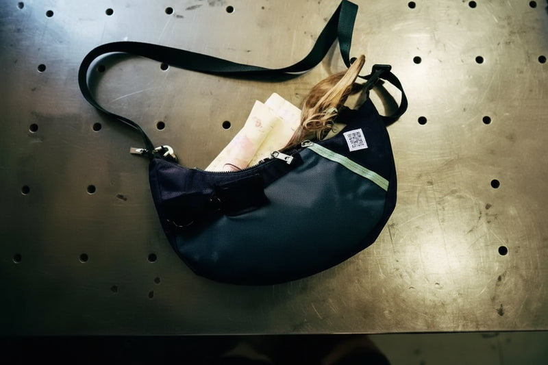 Black shoulder bag with a light green zipper and a white tag on a metal surface