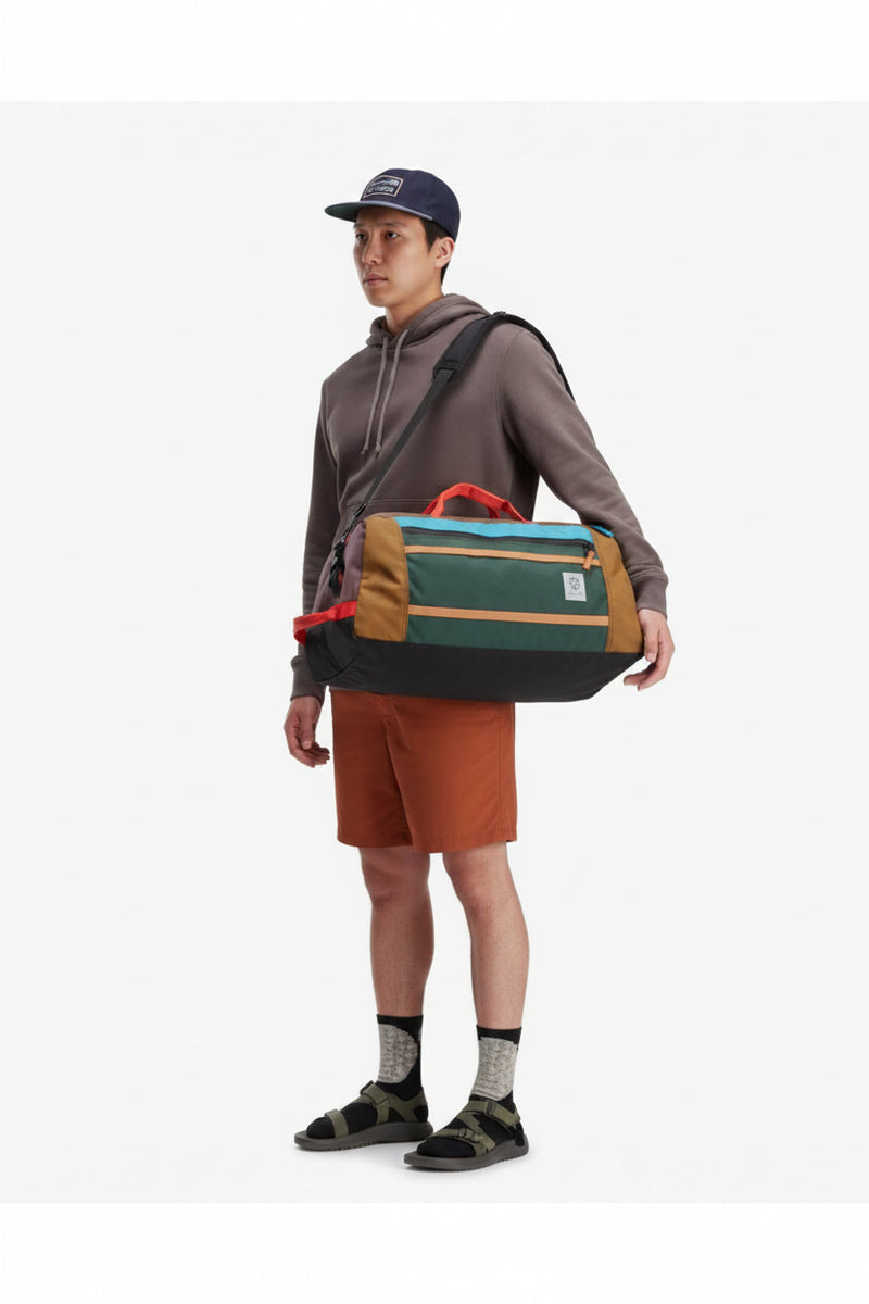 Man wearing a baseball cap, hoodie, shorts, and sandals, carrying a green and brown duffel bag