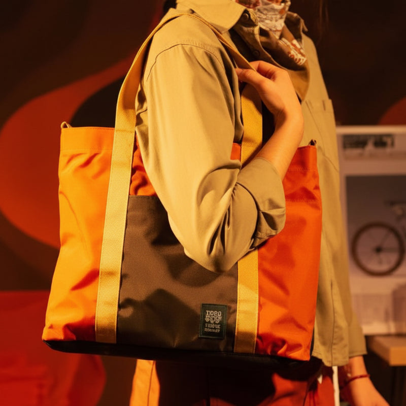 Person wearing a tan shirt and holding an orange and brown tote bag with yellow straps