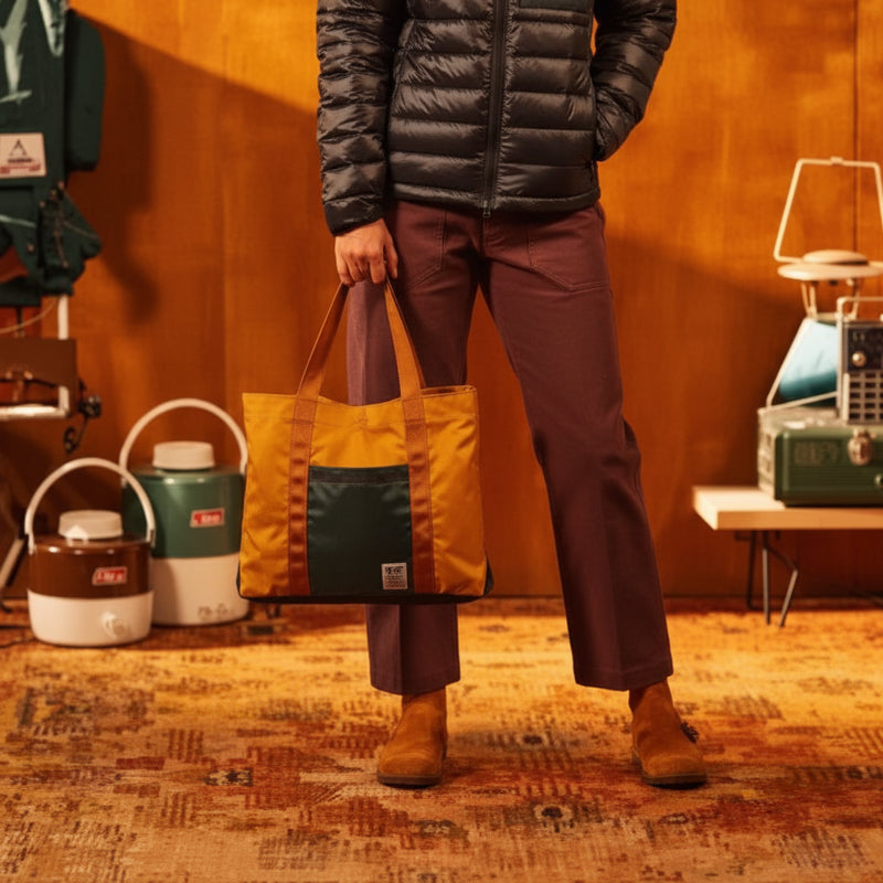Person in black puffer jacket and maroon pants holding a gold and dark green tote bag