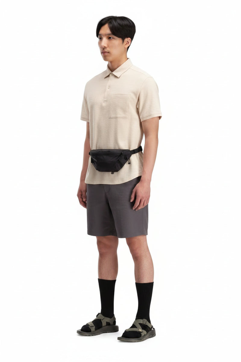 Man wearing a beige polo shirt, grey shorts, black fanny pack, black socks, and green sandals