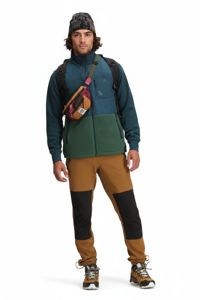Man wearing a blue and green fleece jacket, brown pants with black knee patches, and a patterned beanie