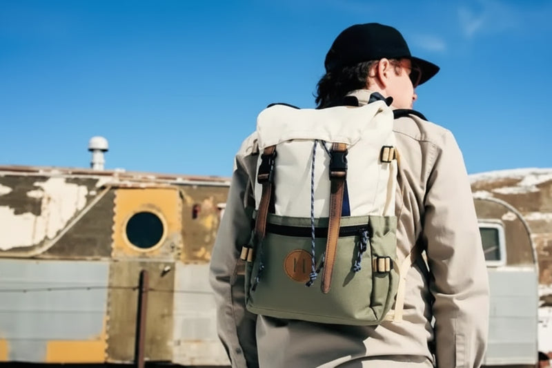 Person wearing a light-colored backpack with brown straps, looking away from the camera