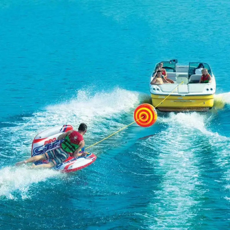 Man on a red and white inflatable tube being pulled by a yellow boat on blue water