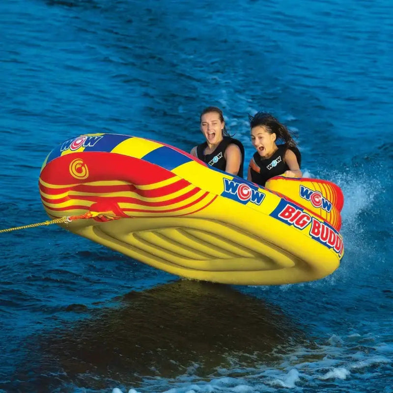 Two women on a yellow and red inflatable tube being pulled by a boat on blue water