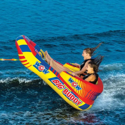 Two women on a yellow and red inflatable tube being pulled by a boat on blue water