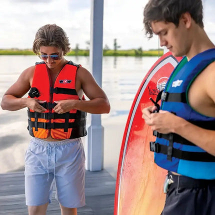 Two men adjusting their life vests on a dock next to a red wakeboard