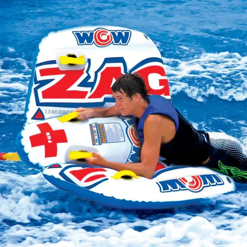 Man on a white, red, and blue inflatable water tube with yellow handles, being pulled through blue water