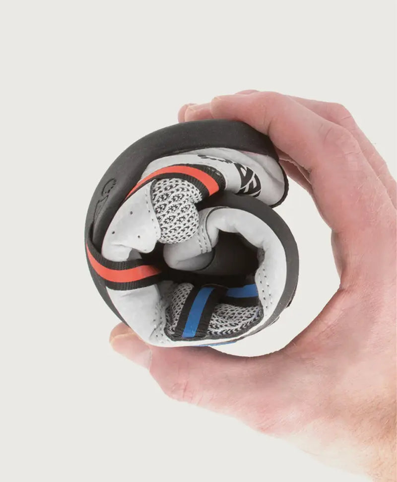 Hand holding a rolled-up white, black, red, and blue athletic shoe